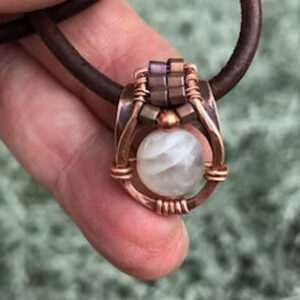 endant-A moonstone bead hanging inside a hammered copper frame